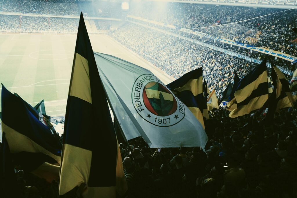 Fans waving Fenerbahce flags in a lively and packed football stadium.
